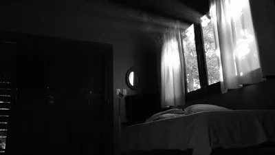 Black and white photo of a bedroom with sunlight streaming through window curtains. Perfect for interior design inspiration.