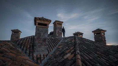 A solitary figure stands on a stone rooftop under a star-filled sky, evoking mystery and adventure.