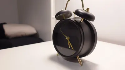 Vintage-style black alarm clock on modern minimalist bedside table in a cozy bedroom.