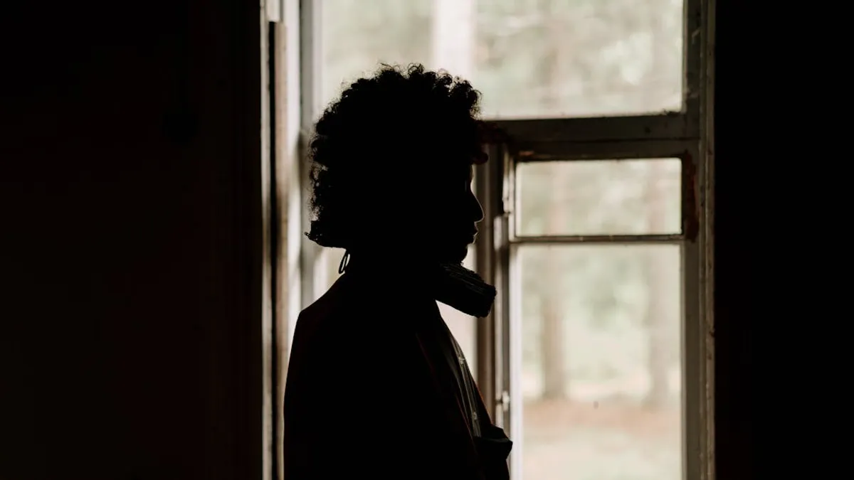 A dramatic silhouette of a person standing by an open window, showcasing introspection and solitude.