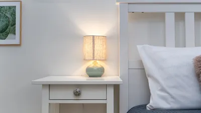 A cozy bedroom setup featuring a lit lamp on a white nightstand beside a bed.