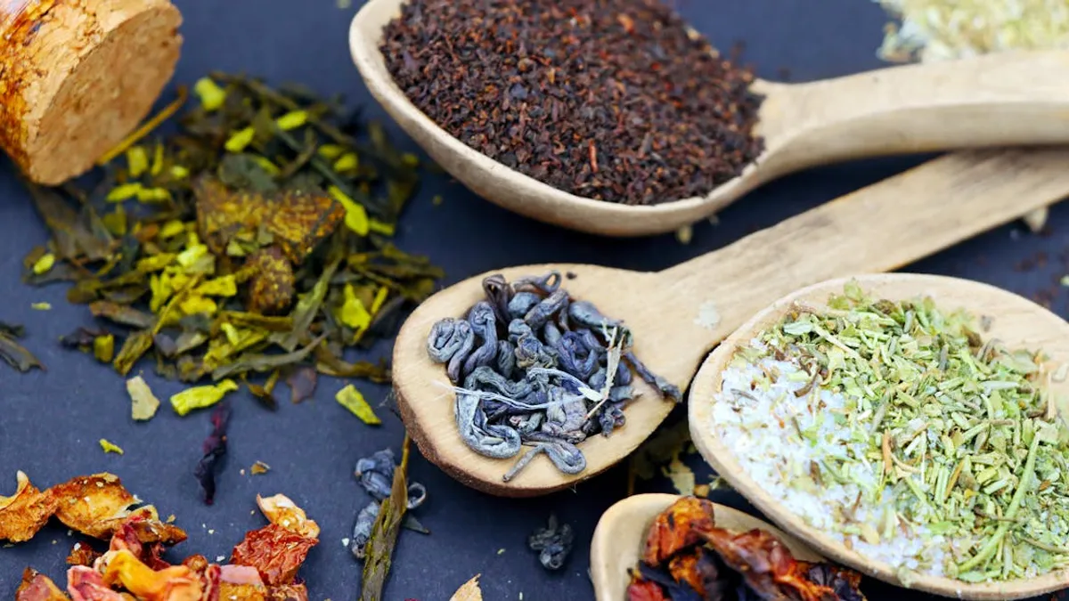 Assorted loose leaf herbal teas in wooden spoons on a flat lay composition, showcasing various colors and textures.