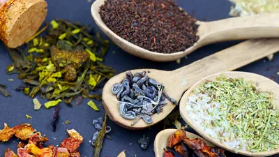 Assorted loose leaf herbal teas in wooden spoons on a flat lay composition, showcasing various colors and textures.
