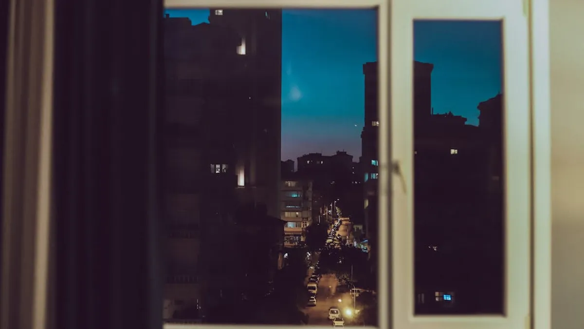 A serene view of an urban street through a window at night with city lights glowing.
