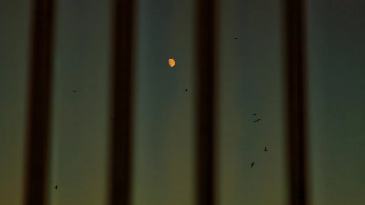 View through dirty window of night sky and moon with shadow from metal bars