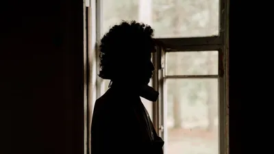 A dramatic silhouette of a person standing by an open window, showcasing introspection and solitude.