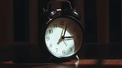 A classic black analog alarm clock illuminated by warm light and artistic shadows.